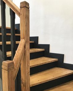 a wooden staircase with black handrails next to a white wall