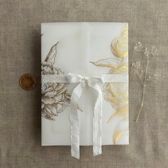 an open gift box with white ribbon and gold foil flowers on the front, sitting on a linen surface