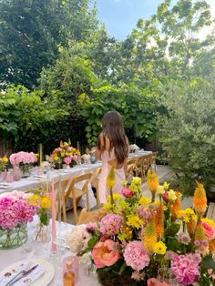 a woman standing in front of a table filled with lots of flowers and greenery