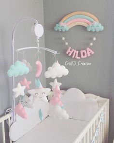 a baby crib with some clouds and stars hanging from it's sides, next to a rainbow sign