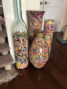 three vases filled with colorful sprinkles on top of a wooden floor