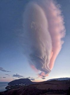 an unusual cloud is seen in the sky over a hill and ocean at sunset or dawn