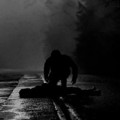 a man kneeling down on the side of a road in the dark with fog behind him