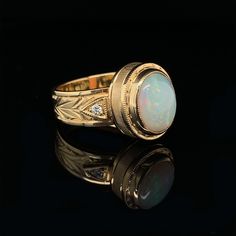 This handmade 18k yellow gold ring features such a pretty opal cabochon! The opal is translucent with a silvery grey body color that provides the perfect backdrop for the opal's play-of-color, also known as "fire." Two sparkling, round brilliant white diamonds complement the opal's bright yellowish-green and violetish blue flashes, while the handmade bezel and band have been intricately hand engraved with exquisite detail. Handmade by our Master Jewelers in Los Angeles, this ring displays attent Ring Displays, Gold Engraving, 18k Yellow Gold Ring, Round Brilliant Cut Diamond, Hand Engraving, Brilliant Cut Diamond, Yellow Gold Rings, Diamond White, Band Rings