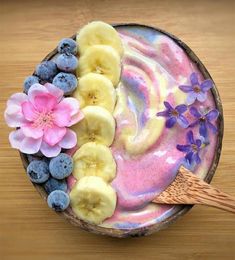 a bowl filled with yogurt, bananas and blueberries on top of a wooden table