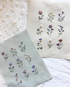 two embroidered napkins with flowers on them sitting on a white tablecloth next to each other