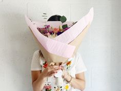 a woman holding a paper bag over her face with flowers on it's head