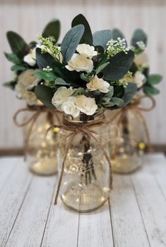 three clear vases with white flowers and greenery tied to each other on a wooden table