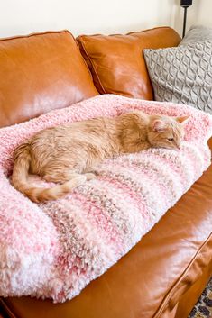 an orange cat sleeping on top of a pink and white blanket in a brown leather couch