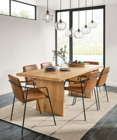 a dining room table with chairs and lights hanging from it's ceiling, in front of a large window