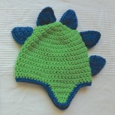 a crocheted green and blue hat laying on top of a white sheet with two ears