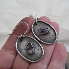 Raw Amethyst Dangle Earrings Rustic Purple Gemstone Hoop Earrings Silver Dangling Earring: Beautiful raw Amethyst points have been captured in hand constructed sterling silver settings.The oval backings have been stamped with a linear pattern and darkened. Each earring is slightly different from the other. They measure about 1 3/4 inches in total length. Truly one-of-a-kind and handmade by me. Enter my shop: https://www.etsy.com/shop/artdi Join me on Facebook: https://www.facebook.com/Artdi-Dian Purple Metal Drop Earrings, Purple Round Metal Earrings, Purple Metal Dangle Earrings, Purple Dangle Metal Earrings, Amethyst Earrings For Gift, Pierced Amethyst Crystal Earrings, Purple Teardrop Metal Earrings, Purple Pierced Metal Jewelry, Purple Metal Pierced Jewelry