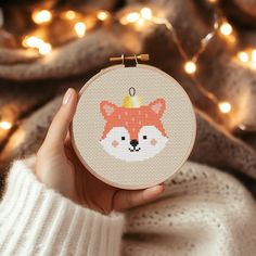 a person holding up a cross stitch fox ornament in front of a christmas tree