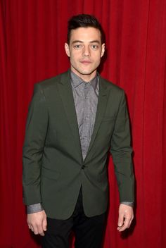 a man in a suit and tie standing next to a red curtain with his hands in his pockets