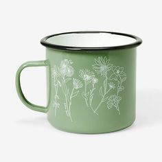 a green enamel mug with white flowers on the outside and black rim, in front of a white background