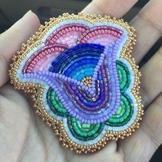 a hand holding a beaded brooch in the shape of a flower with multiple colors