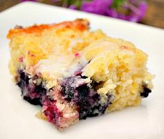 a piece of blueberry cobbler on a plate with purple flowers in the background