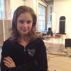 a young woman standing in an office with her arms crossed and looking at the camera