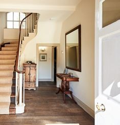 an entry way with stairs, mirror and table next to it in a home that is painted white