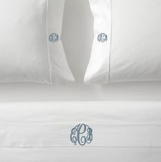 two monogrammed pillows on top of a bed with white sheets and blue trim