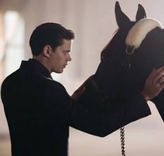 a man in a black suit is petting a horse's bridle