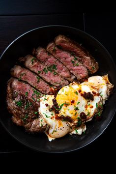 steak, eggs and potatoes are on a black plate