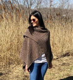 a woman standing in the grass wearing a brown knitted shawl