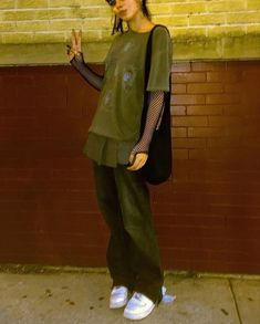 a woman standing in front of a brick wall with her hand up to the side