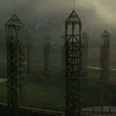 several metal structures in the middle of a grassy area with mountains in the background and foggy sky