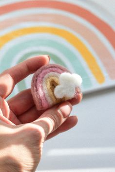 a hand holding a small roll with a white cloud in it's center and rainbow painted background