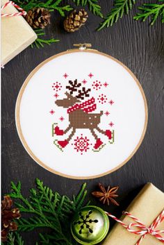 a cross stitch christmas ornament on a table next to presents and pine cones