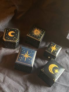 four small boxes with designs on them sitting on a bed next to a pillow and blanket