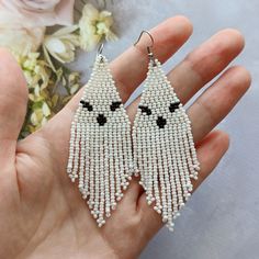 a hand holding a pair of white beaded earrings with black eyes and fringes