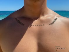 a man with a tattoo on his chest standing in front of the ocean and blue sky