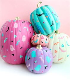 four painted pumpkins sitting next to each other on a white surface with pink and blue background