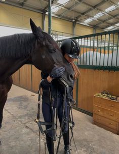 a woman standing next to a brown horse in a stable with its head on the ground