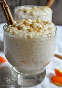 two glasses filled with rice and cinnamon on top of a table next to an orange flower