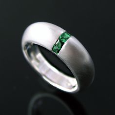 a white gold wedding ring with a green emerald stone in the center, on a black background