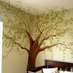 a baby's room with a tree painted on the wall and a teddy bear