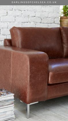 a brown leather couch sitting next to a stack of magazines and a potted plant