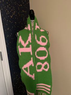 a green and pink knitted sweater hanging on a wall next to a door with the word love written across it