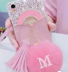 a person holding a pink phone case with a heart and tassels on it