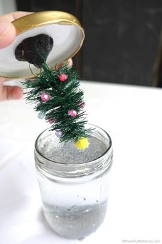 a person is pouring something into a jar with a small christmas tree in the top