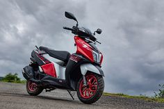 a red and white scooter parked on the side of a road under cloudy skies