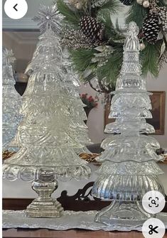 two glass christmas trees sitting on top of a table next to a mirror with pine cones