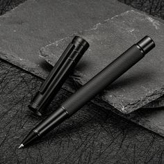 two fountain pens sitting on top of a black piece of paper next to each other