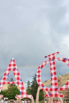 two people holding up red and white checkered letters with a rainbow in the background