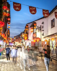 many people are walking down the street in front of buildings with lanterns hanging above them