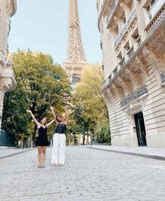 two women standing in front of the eiffel tower with their arms raised up