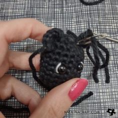 a hand holding a tiny black crocheted animal keychain with eyes on it